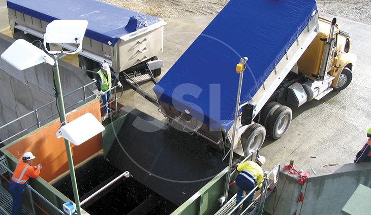 A blue and white dump truck dumping a load of gravel into a large metal container.