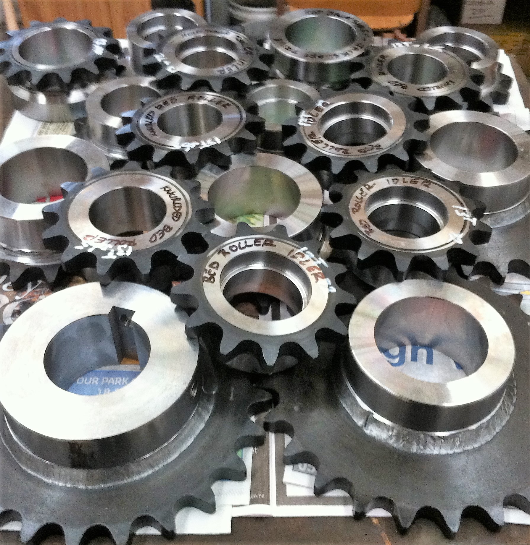 Close-up photo of several metal sprockets with various sizes, hole patterns, and teeth counts, arranged on a metal workbench.