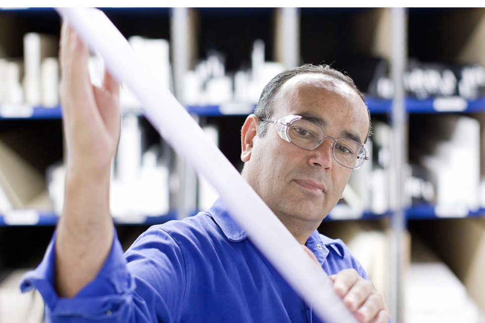 A man wearing glasses and a blue work shirt inspects a rod made from acetal plastic.