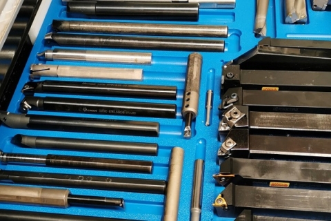 A blue tray filled with various metalworking tools, including lathe chucks, calipers, and drill bits.