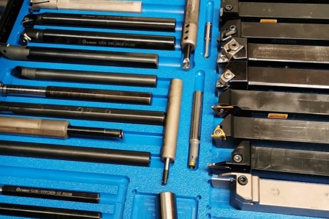 A blue tray filled with various metalworking tools, including lathe chucks, calipers, and drill bits.